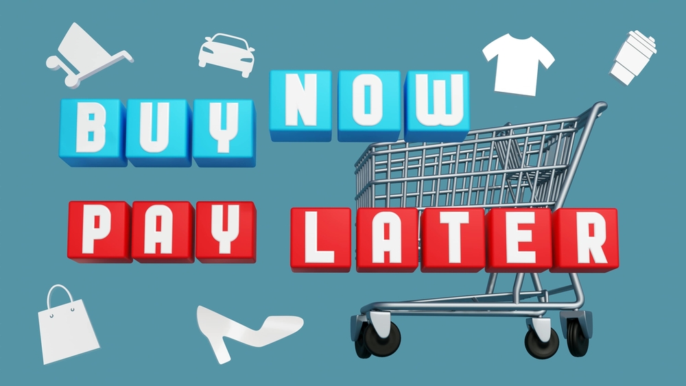 A shopping cart with 3D blocks spelling Buy Now Pay Later. Surrounding icons include a car, stroller, shirt, coffee cup, shoe, bag, and gift. Blue background.