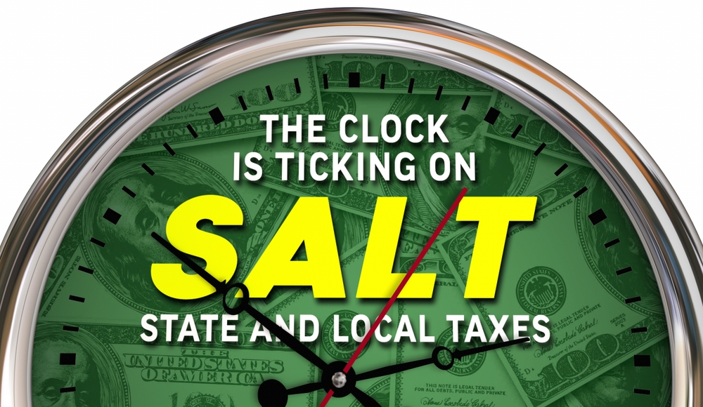 A clock face with U.S. dollar bills in the background and the words THE CLOCK IS TICKING ON SALT STATE AND LOCAL TAXES written prominently across the center.