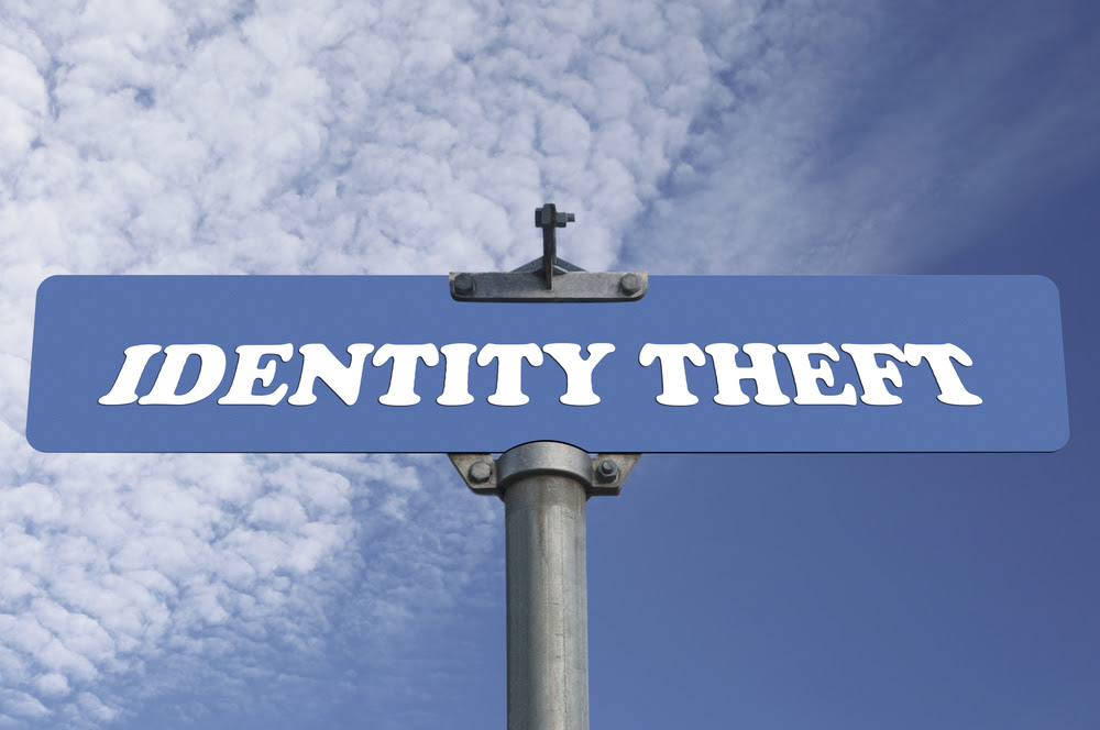 A blue street sign with the words IDENTITY THEFT in white capital letters against a cloudy sky background.