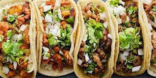 Four street-style tacos with corn tortillas, filled with seasoned meat, chopped onions, and fresh cilantro, arranged side by side.
