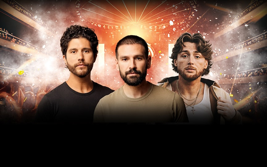 Three men stand in front of a dramatic, glowing background with an audience and stage lights, giving a concert-like atmosphere. The men have serious expressions and are dressed in casual clothing.