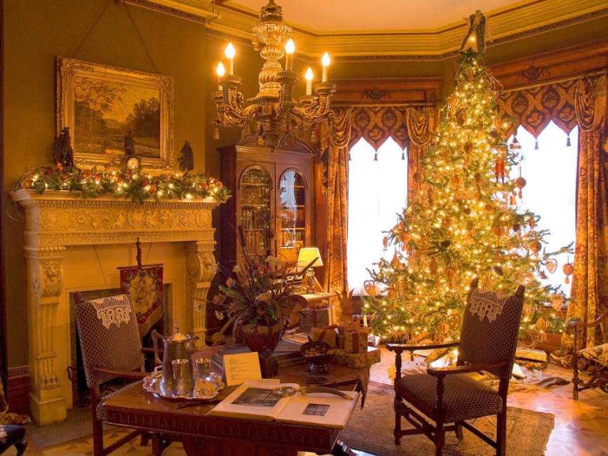 A warmly lit living room decorated for Christmas, featuring a glowing Christmas tree, an ornate fireplace with garlands, elegant furniture, a chandelier, and a festive, cozy atmosphere.